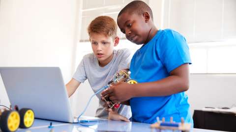 兩名中學生站在教室工作台前協作，面前是一部筆記型電腦，用來編寫連線的 Arduino 裝置。