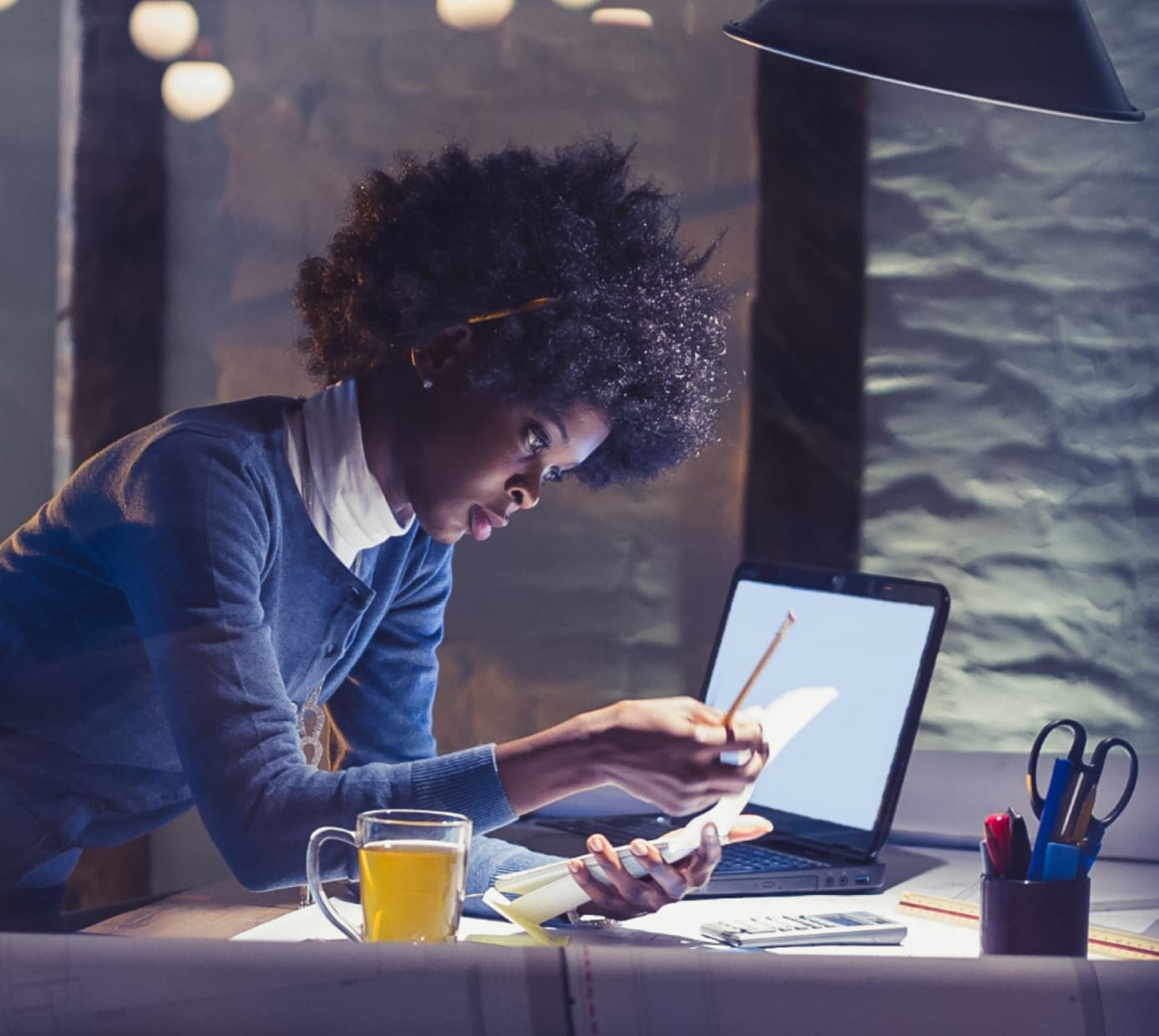 一位女性專業人士獨自在空無一人的辦公室工作，旁邊有一杯茶和一台筆記型電腦。